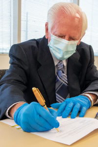 Man in medical mask and gloves signing endowment documents during COVID pandemic