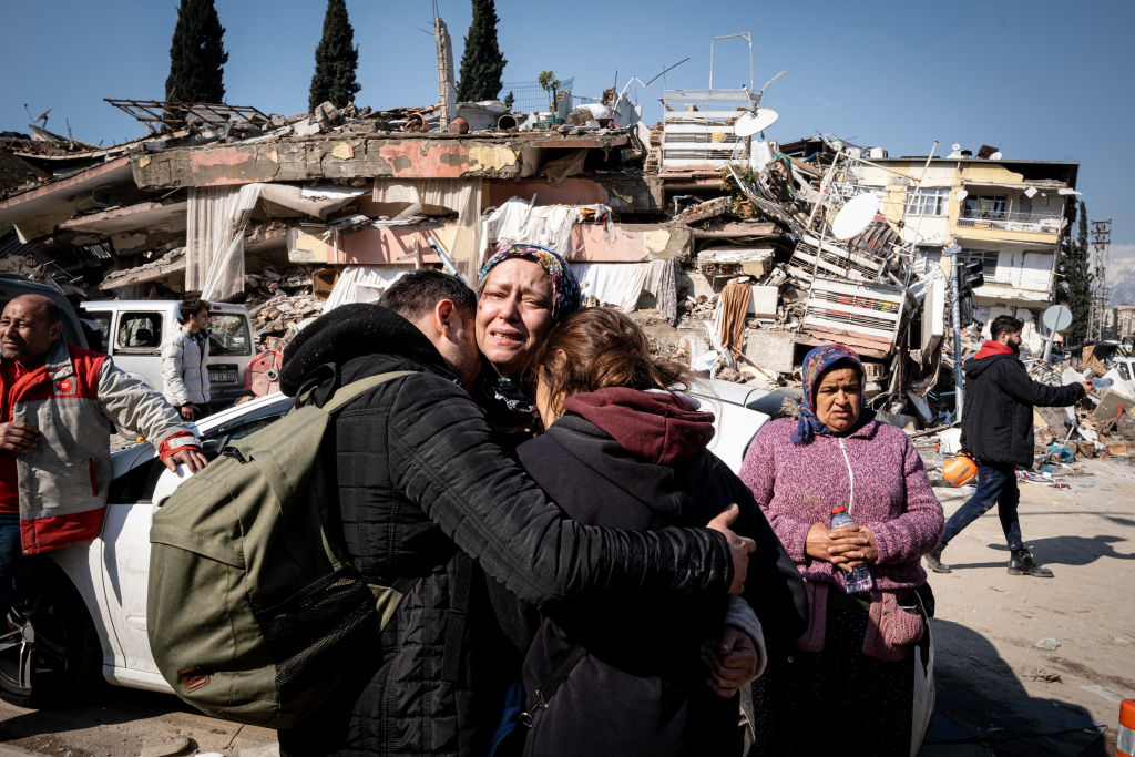 Image of family hugging in front of destroyed building.