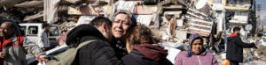 Image of family hugging in front of destroyed building.